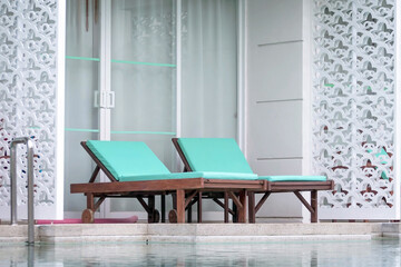 Wooden loungers with soft mattresses in pastel color by swimming pool