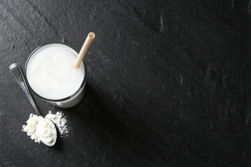 Delicious protein shake in glass and spoon with powder on black table, top view. Space for text