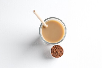 Delicious protein shake in glass and scoop with powder on white background, top view