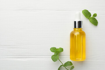 Bottle of essential oil and mint on white wooden table, flat lay. Space for text