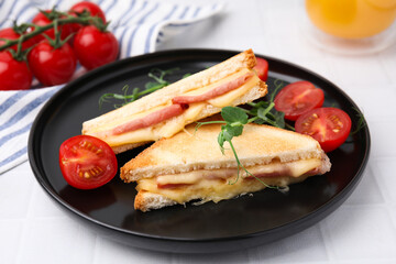 Pieces of toasted bread with melted cheese, ham and tomatoes on white tiled table