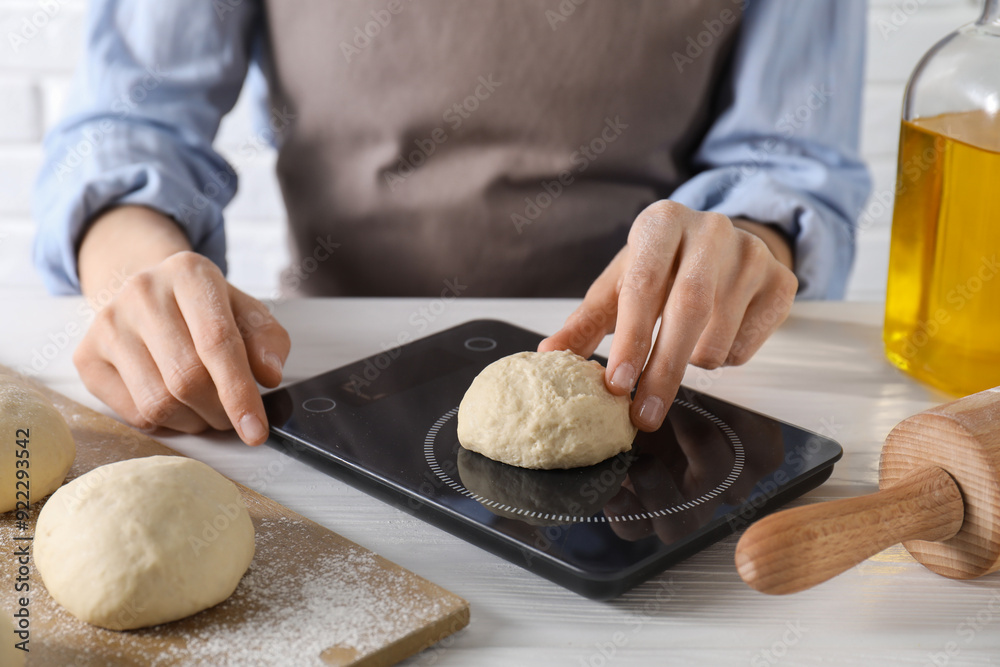 Wall mural woman weighing raw dough ball on kitchen scale at white wooden table, closeup