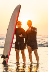 Two friends making hand gestures with surfboards