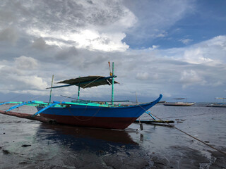 Fototapeta premium Beautiful view of a boat anchored by the sea on a bright, sunny, and cloudy day.