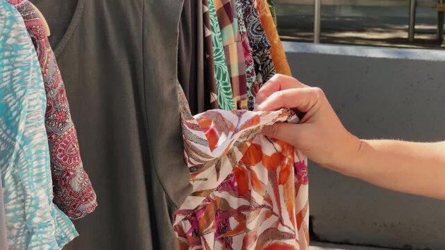 Woman choosing a dress in a vintage second hand clothing store, female hands sort through clothes on a hanger.