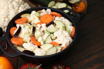 Cooking stew. Cut raw vegetables in pot on wooden table, closeup