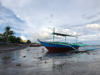 Fototapeta premium Beautiful view of a boat anchored by the sea on a bright, sunny, and cloudy day.