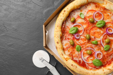 Delicious vegetarian pizza in box and cutter on black table, top view. Space for text