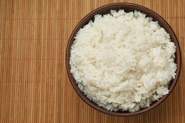 Tasty cooked rice in bowl on bamboo mat, top view. Space for text