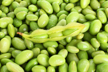 Raw green edamame pod on soybeans as background, top view