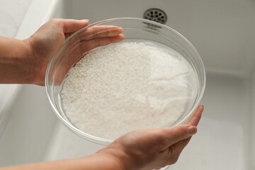 Woman holding bowl with rice and water above sink, closeup