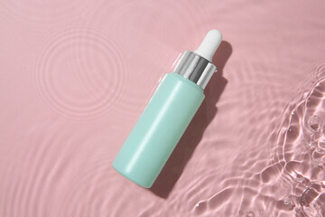 Bottle of cosmetic product in water on pink background, top view