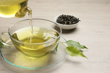 Pouring refreshing green tea into cup at wooden table, closeup