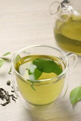 Refreshing green tea in cup, teapot and leaves on wooden table, closeup