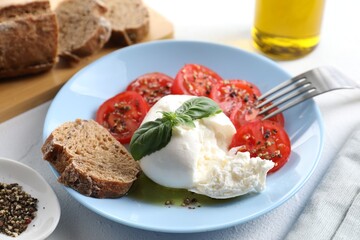 Delicious burrata cheese, tomatoes, basil, bread and spices on white table, closeup