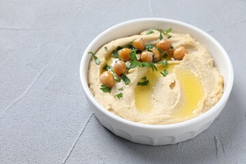 Delicious hummus with olive oil, chickpeas and parsley in bowl on grey textured table