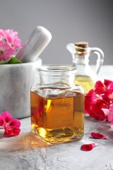 Geranium essential oil and beautiful flowers on light grey textured table