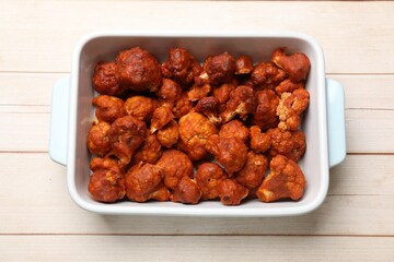 Baked cauliflower buffalo wings in baking dish on wooden table, top view