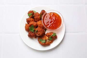 Baked cauliflower buffalo wings with parsley and sauce on white tiled table, top view