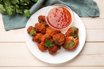 Baked cauliflower buffalo wings with parsley and sauce on wooden table, flat lay