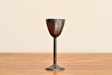 Antique weathered copper goblet with high stem on the brown wooden table. Close-up. Copy space.