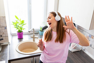 Happy woman singing in kitchen with headphones