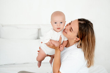 a young beautiful mother with a baby boy hugging on the bed at home in the bedroom, mother's care and love, portrait of a happy mother with a child, healthy motherhood