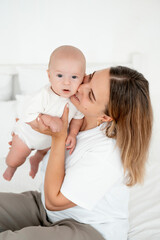 a young beautiful mother with a baby boy hugging on the bed at home in the bedroom, mother's care and love, portrait of a happy mother with a child, healthy motherhood