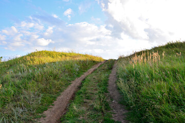 a dirt road is going up the hill with sunlight and some white clouds