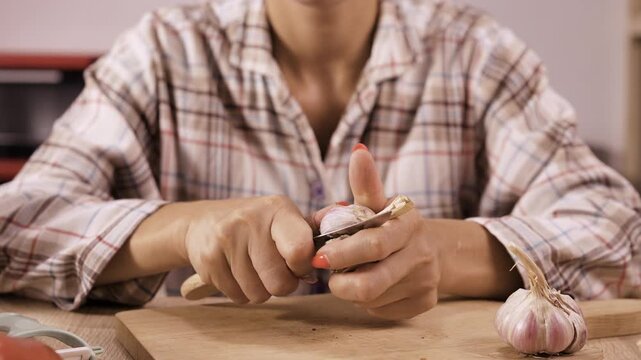 Woman peeling garlic by hand and with knife for cooking on home kitchen