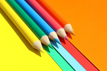 Multi-colored bright pencils lie on multi-colored paper.