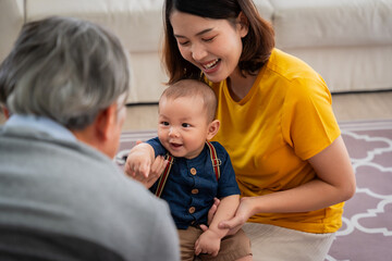 Obraz premium A man and a woman are playing with a baby in a living room. The baby is holding a toy and smiling. The scene is warm and friendly, with the family enjoying each other's company