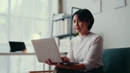 Young woman typing on a laptop, then taking a break and contemplating, in a bright, modern office setting with shelves and soft lighting