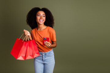Photo of charming positive woman wear orange t-shirt typing modern gadget rising shoppers empty space isolated khaki color background
