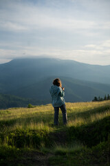 a woman with camera alone, smiling, happy, in the mountains, silhouettes of mountains on the background , in the forest, tourism, hiking, independence, overcoming fears, beauty of nature, solo hiking