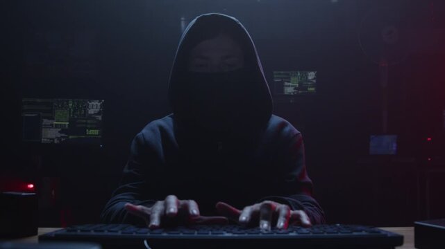 A cloaked figure works intently on a computer in a dim room, embodying the essence of cybersecurity
