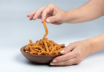 Studio shot of female hands holding a carved wooden bowl containing a heap of soy stick snakcs,...