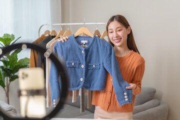 social media market concept. Young Asian woman seller showing second-hand clothes during live...