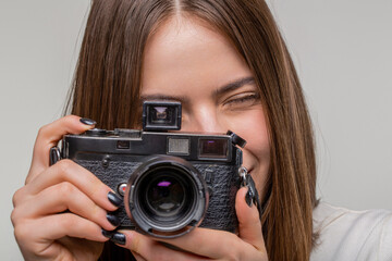 Beautiful young woman photographing on retro camera isolated on gray background. Professional photographer working. Girl using a camera photo. Girl with a cameras, close up.