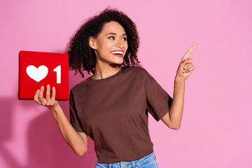 Photo of adorable pretty positive girl wear brown stylish clothes hold red card look empty space isolated on pink color background