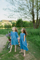 Fototapeta premium sisters with bicycle and flowers and summer wind 