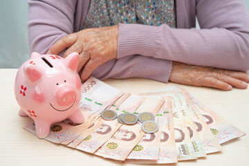 Asian elderly woman with pink piggy bank for saving money and insurance, poverty, financial problem...