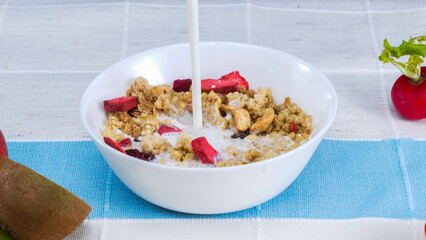 Close up of a white bowl of cereal with milk being poured into it. Macrography of white milk pouring in to bowl with cornflake, dry fruit and splashing milk with isolated white background. Pabulum.