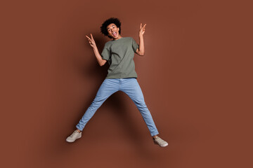Full size photo of nice young guy jump show v-sign wear trendy khaki outfit isolated on brown color background