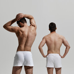 Rear view photo of two young men posing shirtless showing their healthy backs and postures against...