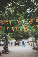shot of city street decorated with small colorful flags, walking people in the street. Decorative multi-colored flags against the city background