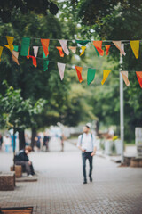 shot of city street decorated with small colorful flags, walking people in the street. Decorative...