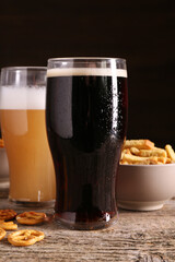 Glasses of beer, pretzel crackers and rusks on wooden table, closeup