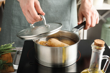 Woman boiling potatoes in saucepan on stove, closeup