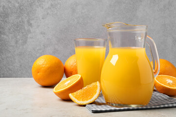 Tasty orange juice in jug, glass and citrus fruits on light table. Space for text
